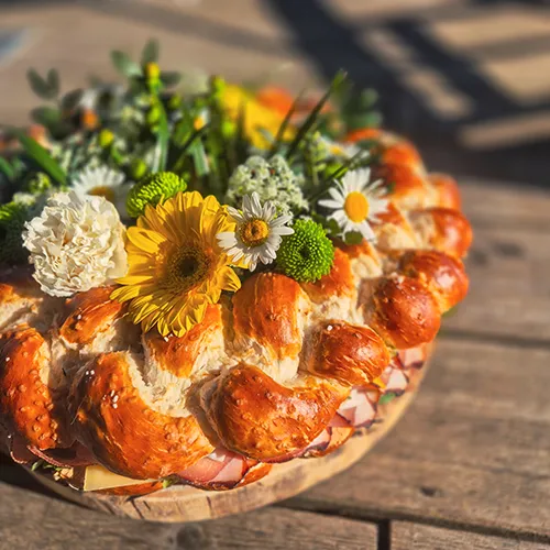 Geflochtenes Brot mit Schinken-Käse-Füllung, verziert mit Sommerblumenstrauß – herzhaftes Gebäck von Kostbarkeiten
