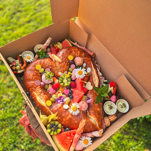 Herzförmige Laugenstange gefüllt mit Schinken, dekoriert mit Obst, essbaren Blüten und Macarons in Box – Picknick-Box von Kostbarkeiten
