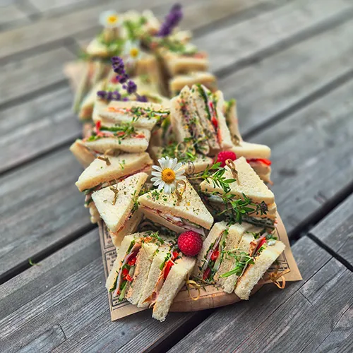 Bunte Sandwich-Häppchen mit essbaren Blüten, Kresse und Beeren auf Holzbrett – Fingerfood von Kostbarkeiten